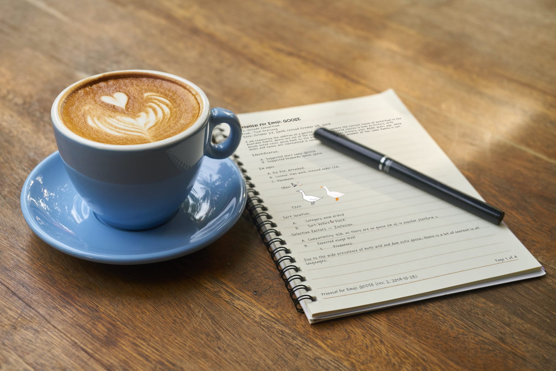 Photo of a paper notebook next to a cup of coffee on a wooden table surface.