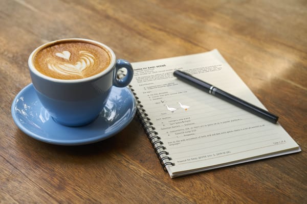 Photo of a paper notebook next to a cup of coffee on a wooden table surface.